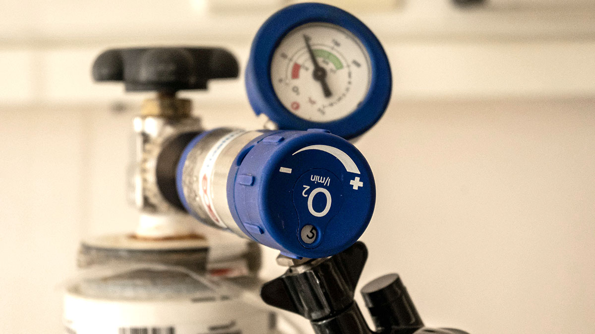 Close-up photo of an oxygen tank showing the pressure gauge and the blue valve controlling oxygen flow.